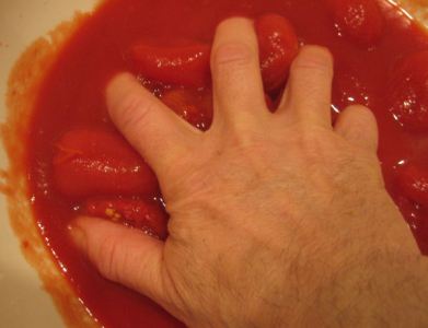 hand mashing tomatoes for pizza sauce